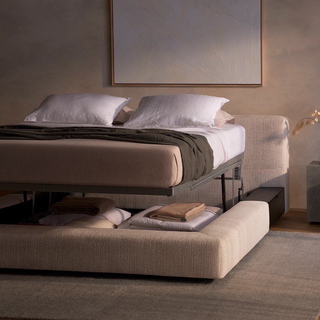 Lift-up bed with storage underneath containing folded linens in a neutral bedroom