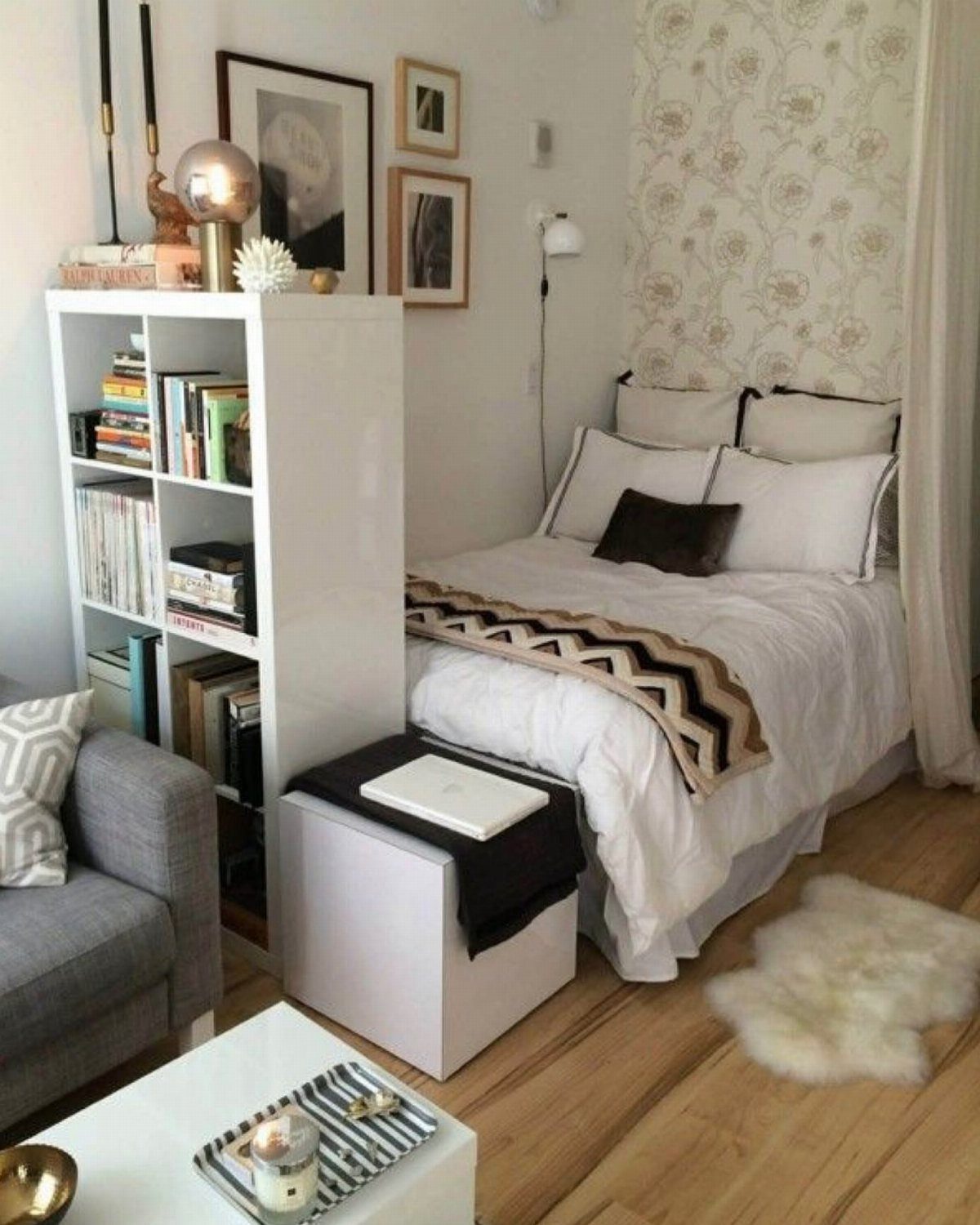 Bed separated from a living area by a white bookshelf in a studio.