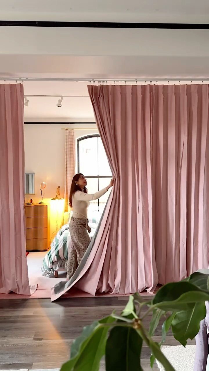 Woman pulling back pink curtains used as a room divider between living and bedroom.