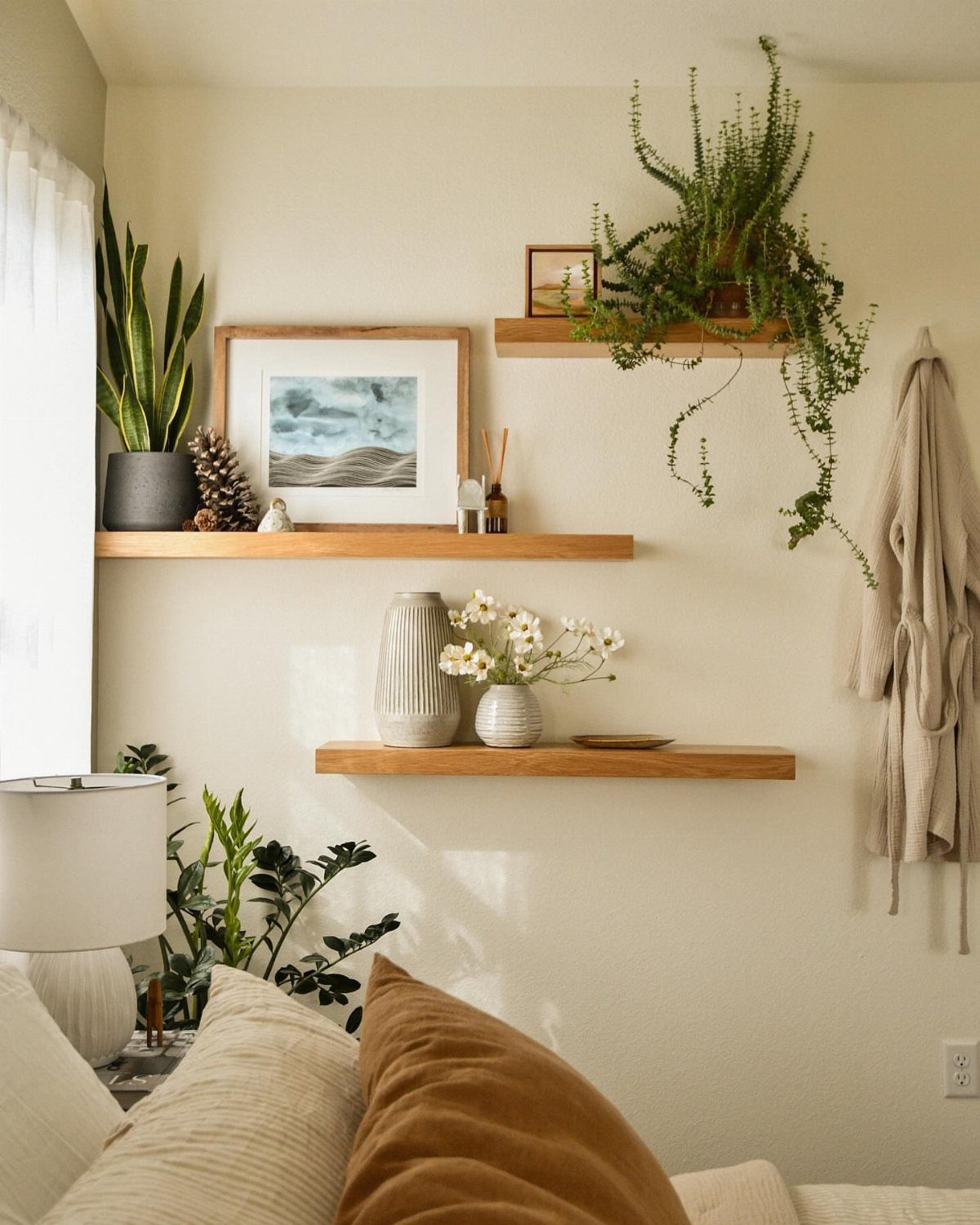 Wooden floating shelves on a cream wall holding plants, art, and ceramic vases.