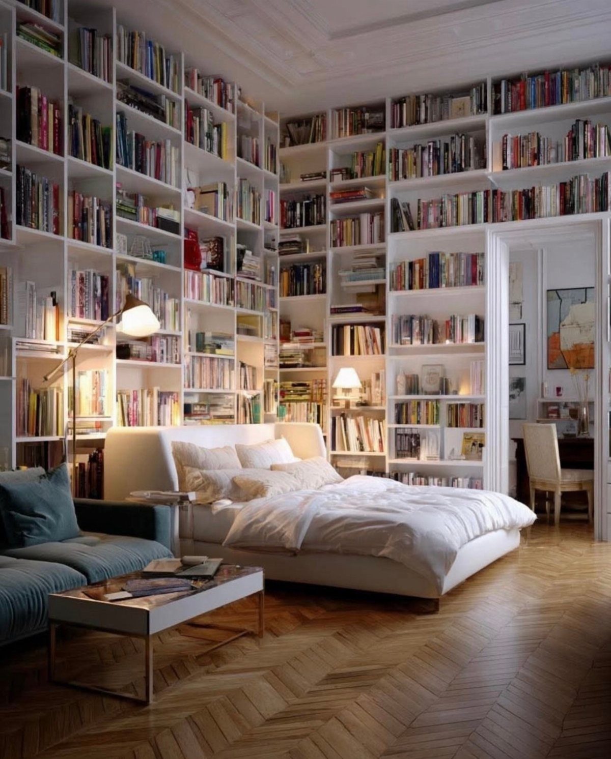 White bed and blue sofa in a room with floor-to-ceiling bookshelves.
