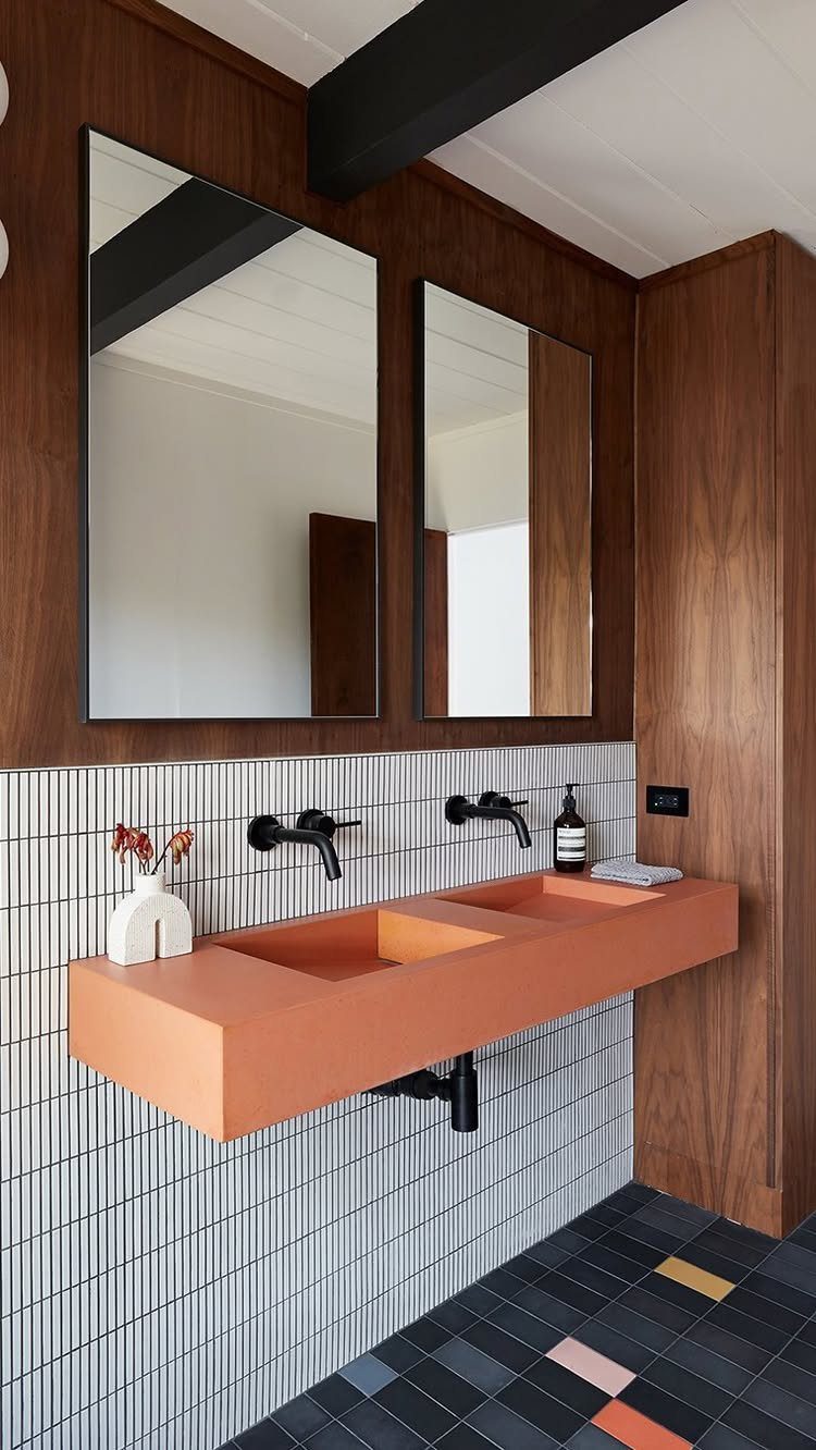 Orange floating double vanity with black faucets against white tiled walls and wood paneling.
