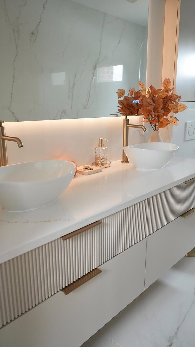 White bathroom vanity with fluted cabinet doors, gold hardware, and two vessel sinks.