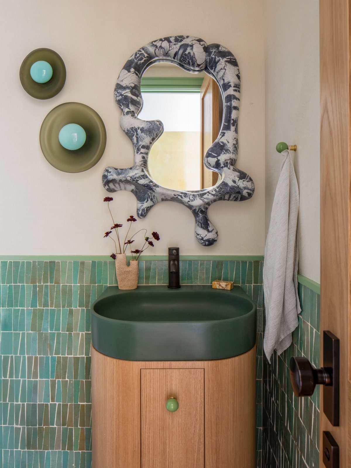 Green integrated sink on a light wood vanity with teal mosaic wall tiles.