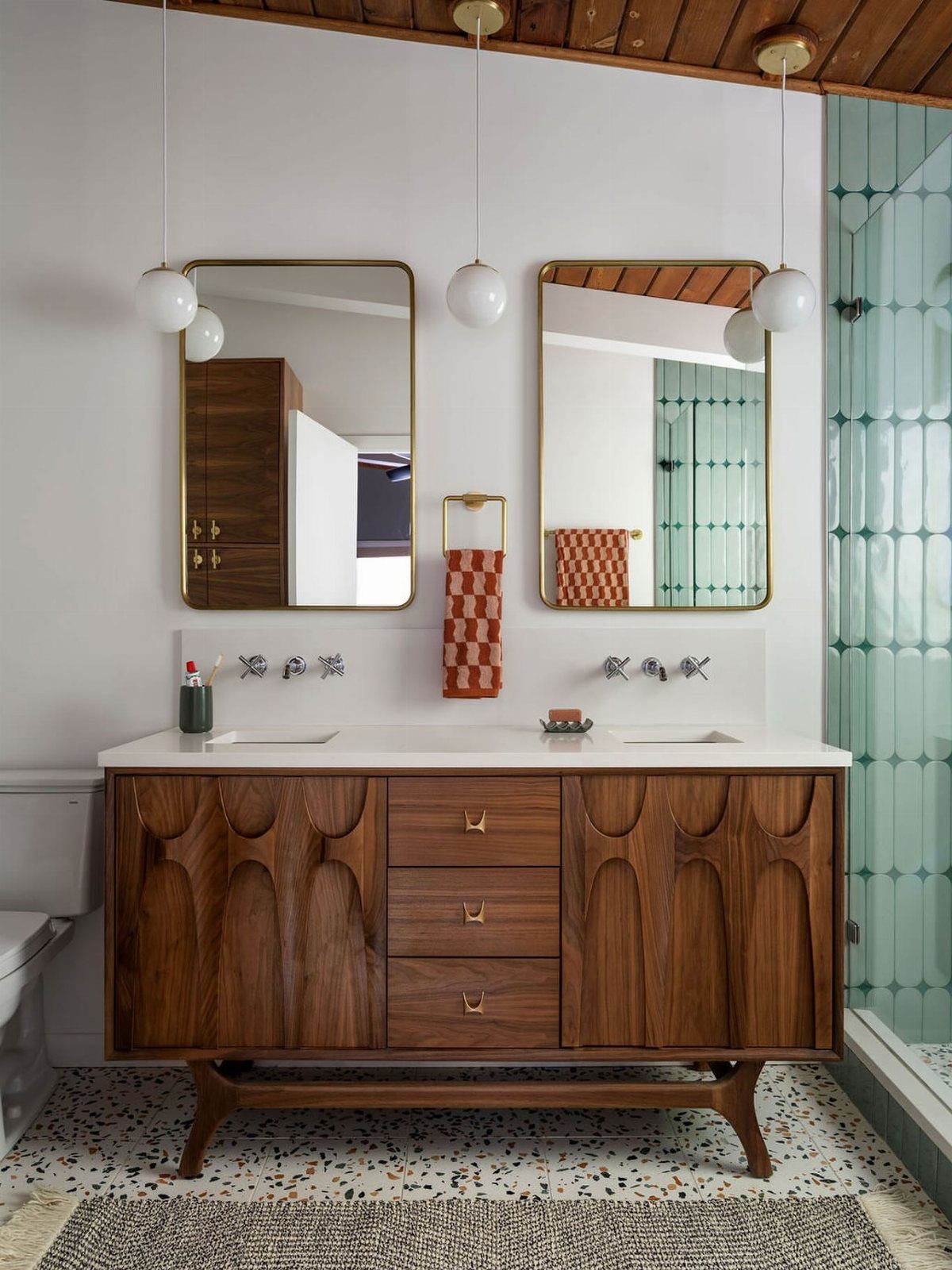 Walnut bathroom vanity with carved doors and tapered legs on terrazzo flooring.