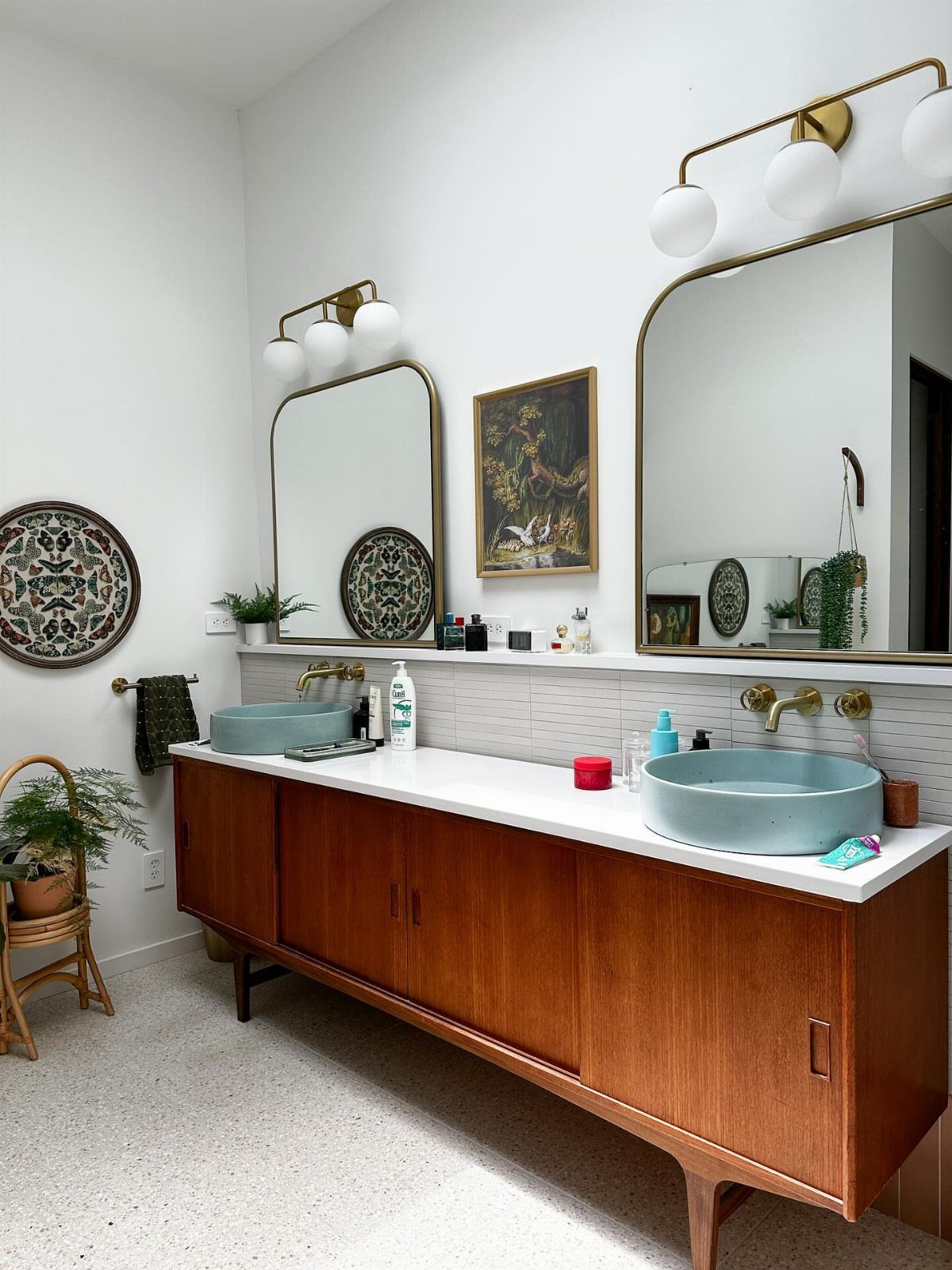 Two light blue vessel sinks on a walnut wood vanity with gold hardware.