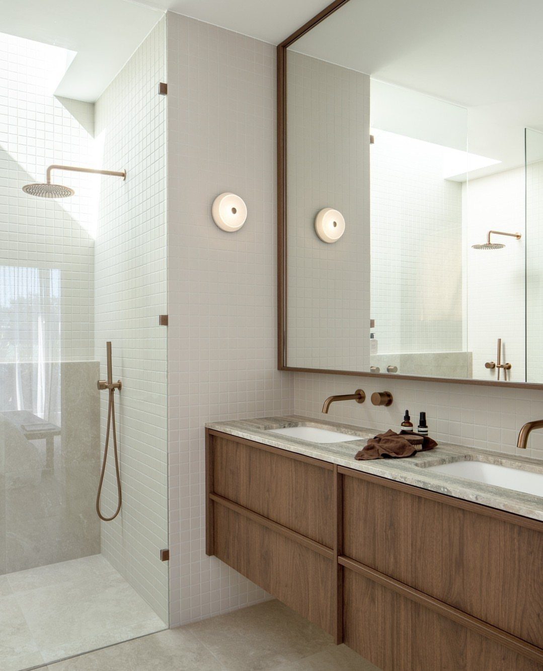 Walnut wood floating bathroom vanity with double sinks and gold fixtures in bright room.
