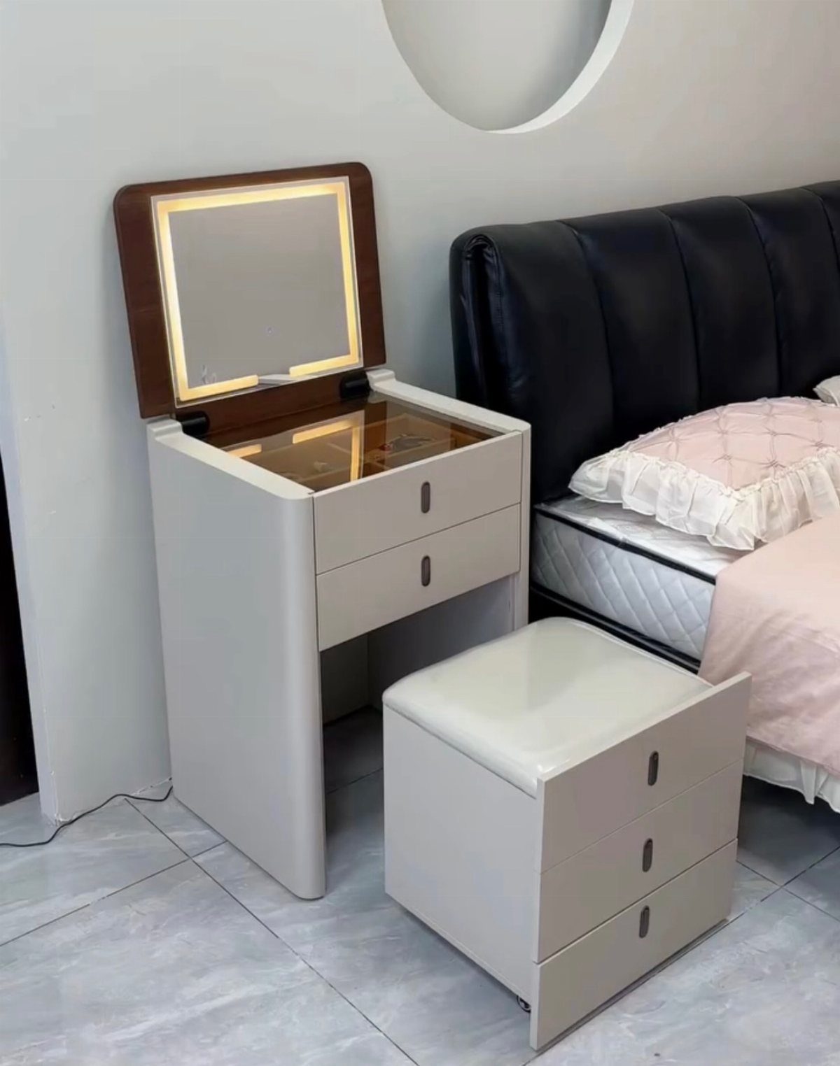 White compact dressing table with flip-top mirror and matching storage stool next to bed.